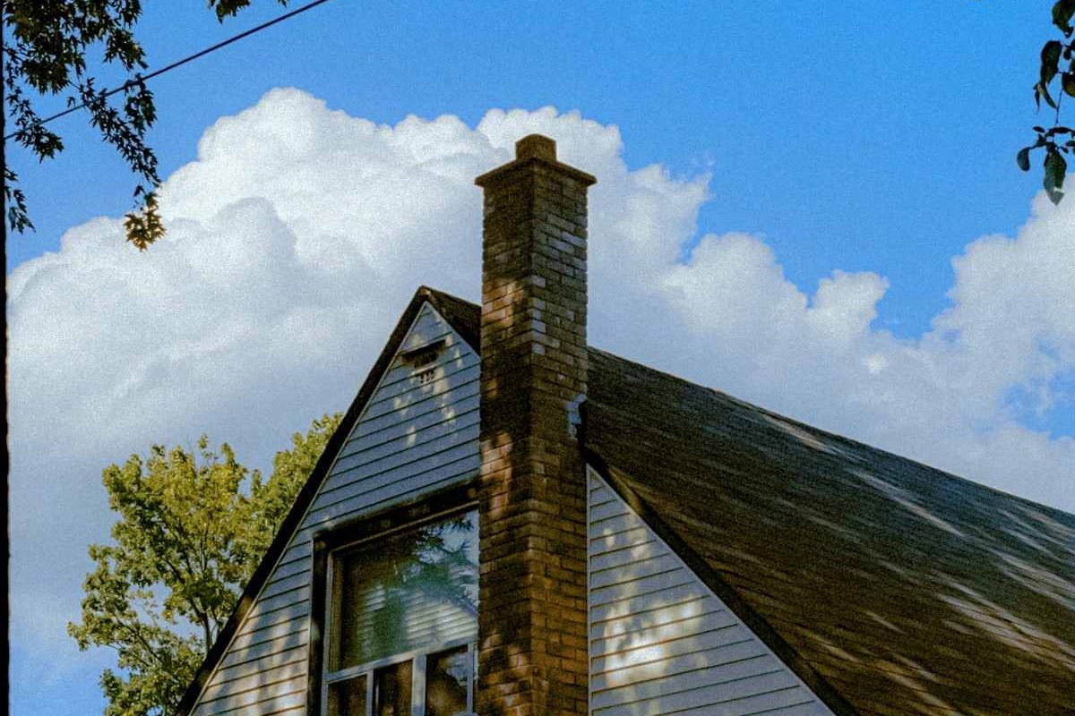 A brick chimney beside a shingle roof under building summer clouds