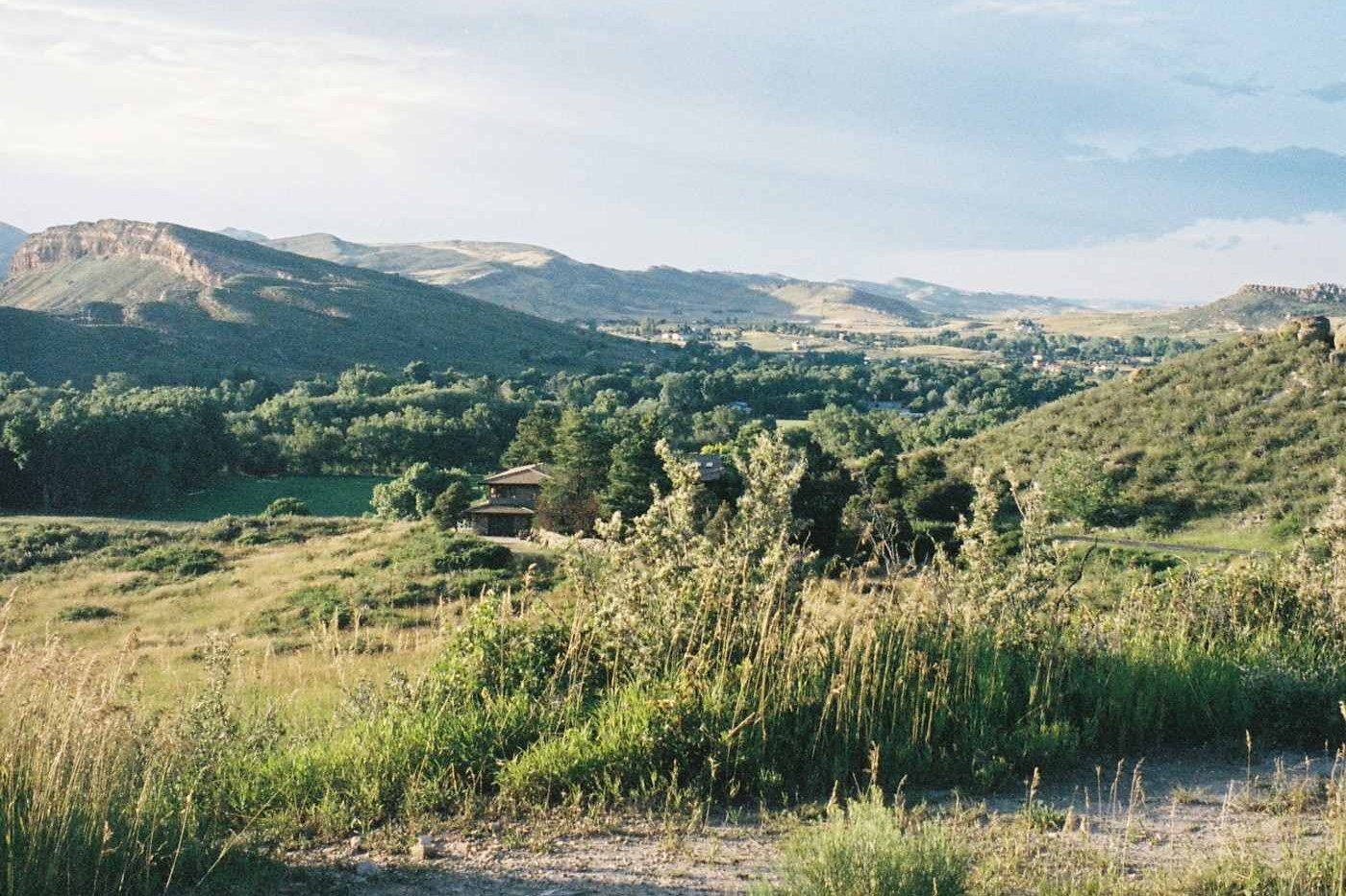 Grassy foothills with scattered homes and a rocky ridge on the horizon