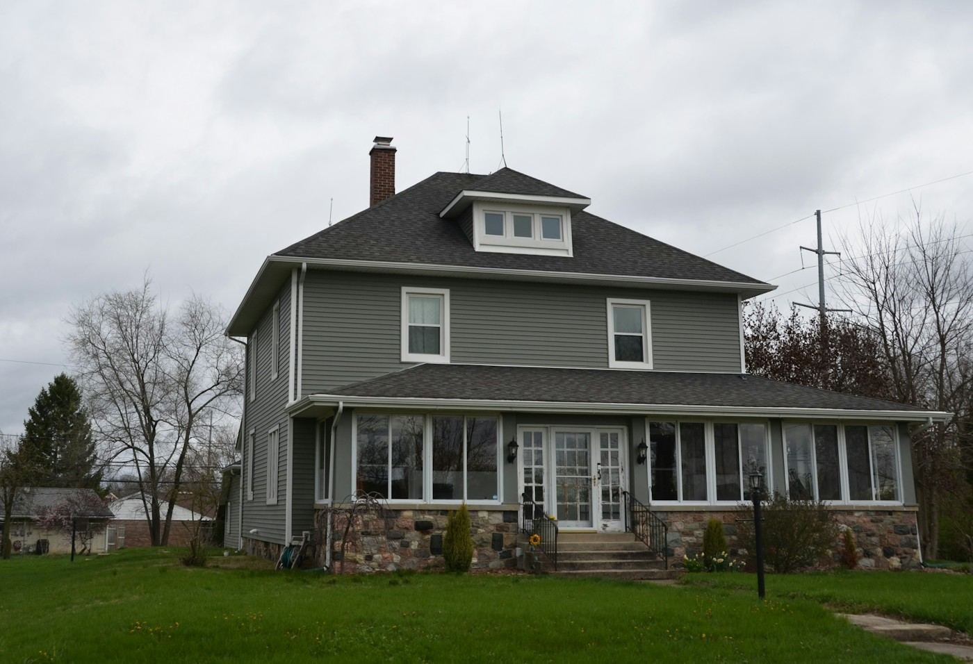 A gray two-story house with a stone base and an enclosed front porch