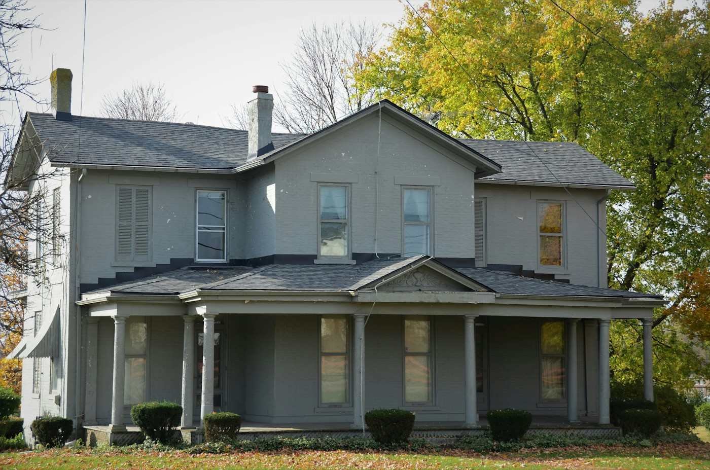 A gray two-story house with a long front porch and a dark shingle roof