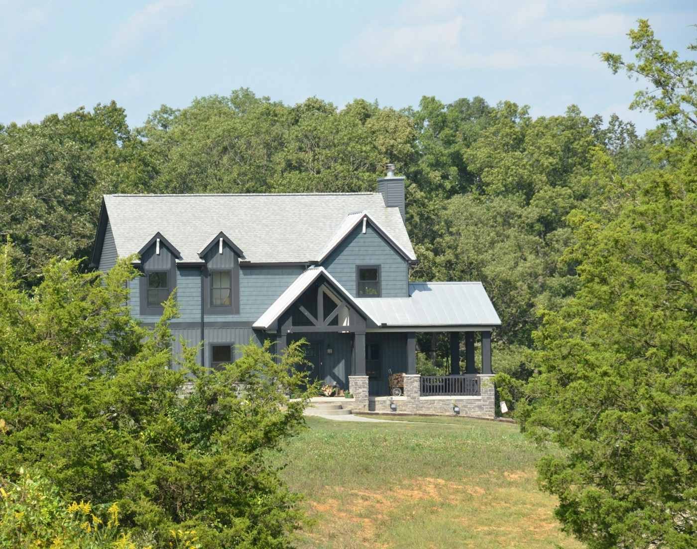 A gray two-story house with gabled dormers on a wooded lot