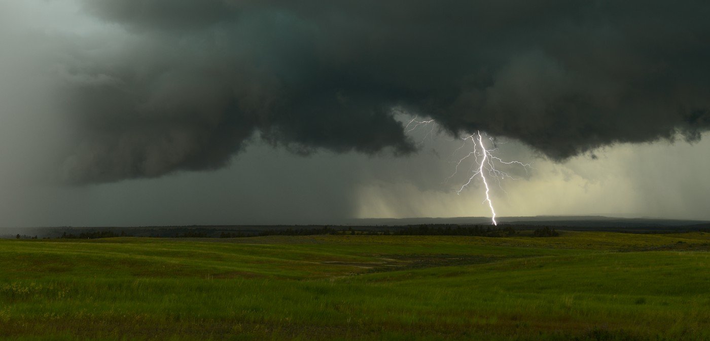 A lightning bolt under a low storm cloud over green fields