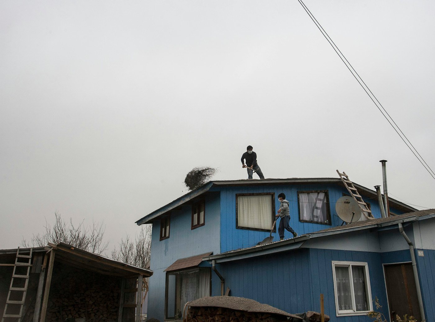 Two roofers working on the roof of a blue two-story house